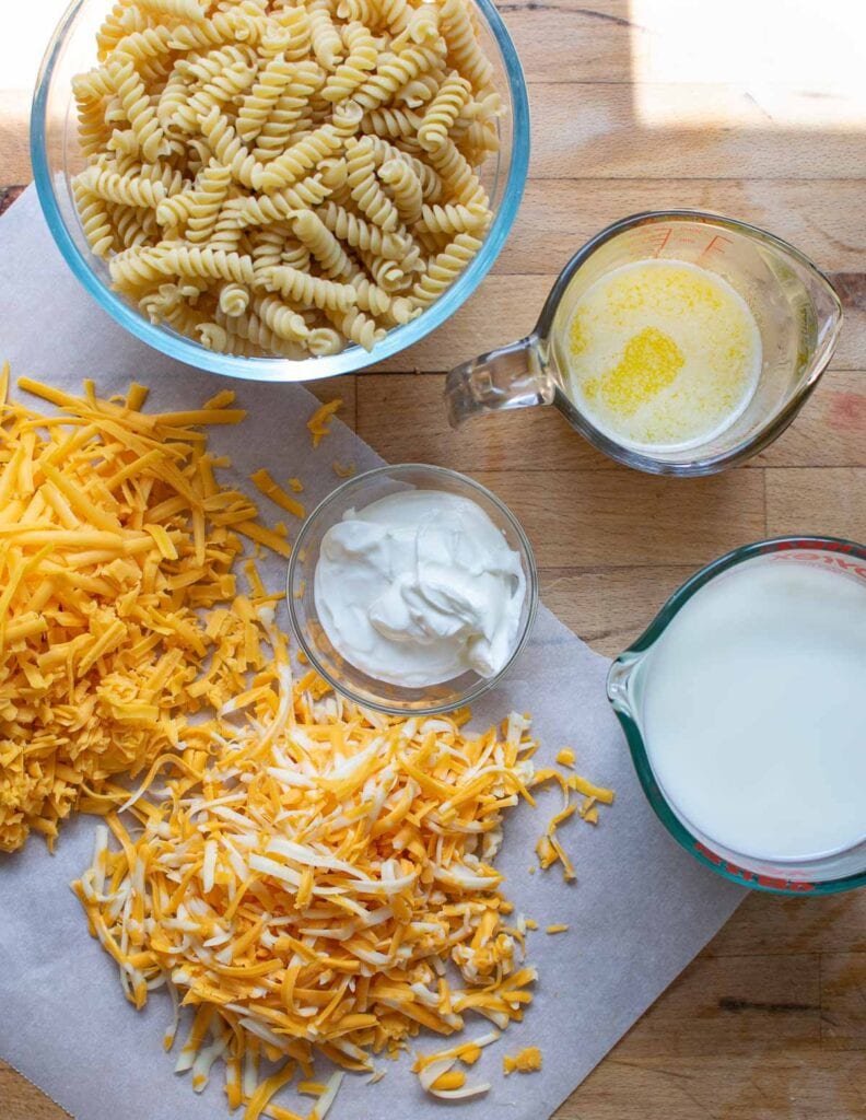 Ingredients to make slow cooker macaroni and cheese including milk, cheese, sour cream, butter and spiral pasta.