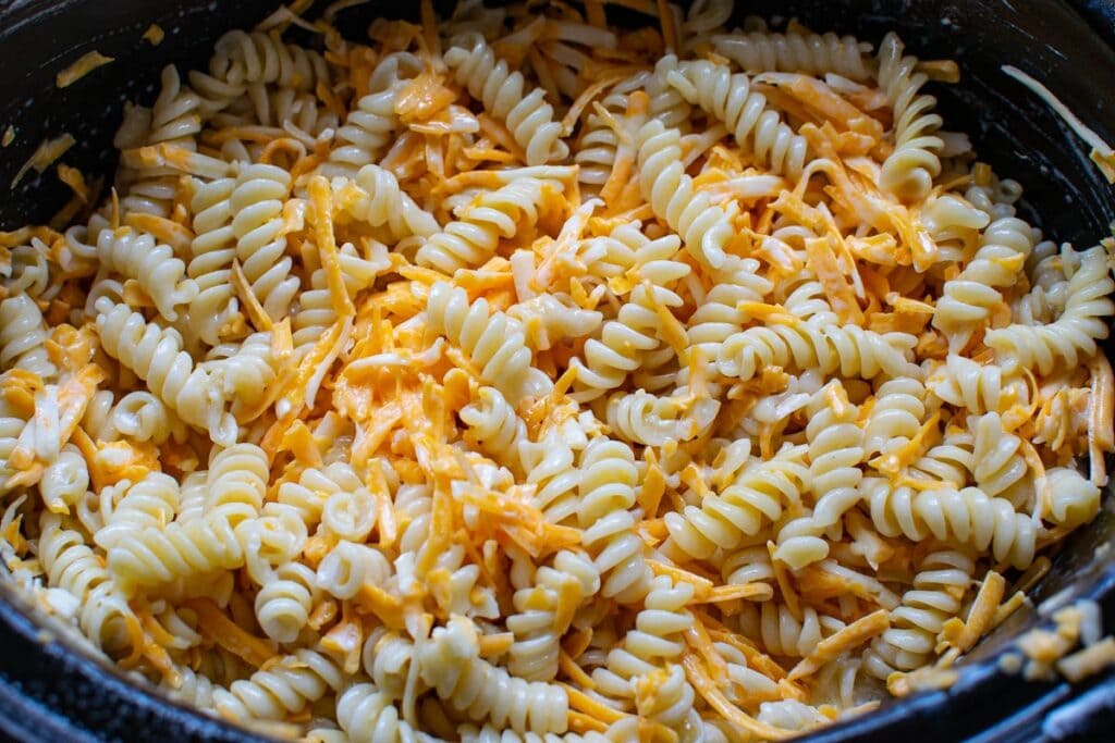 Shredded cheddar cheese added to pasta and cream mixture to make macaroni and cheese in a slow cooker.