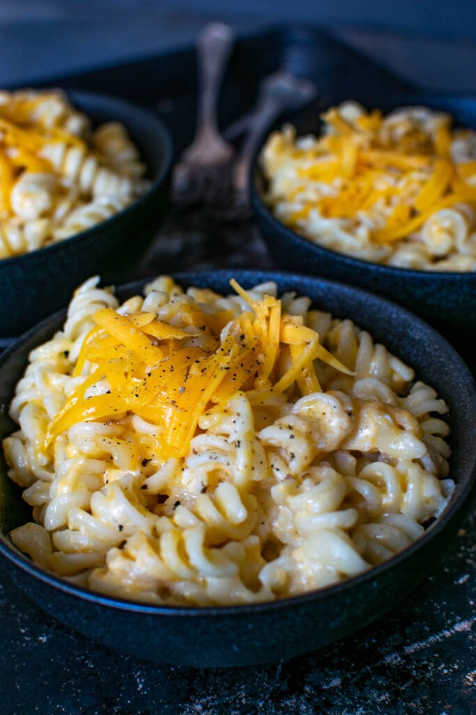 3 bowls of macaroni and cheese made with spiral noodles and sprinkled with shredded cheddar.
