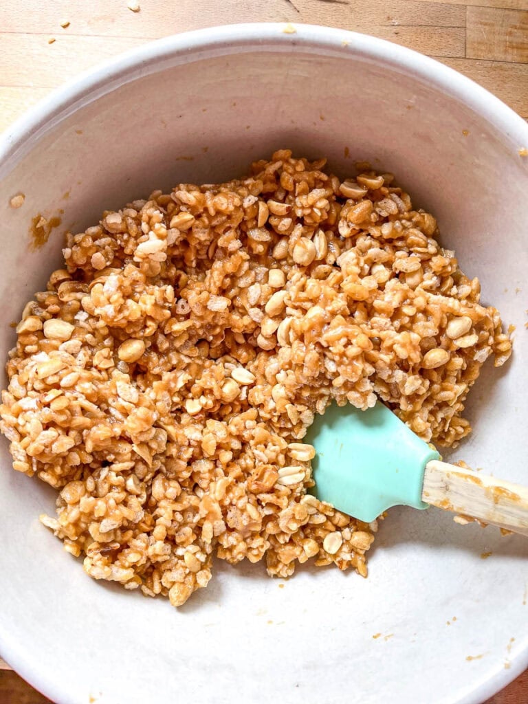 In a large mixing bowl Rice Krispie cereal and peanuts stirred into a mixture of melted peanut butter and corn syrup to make sweet Marie bars.