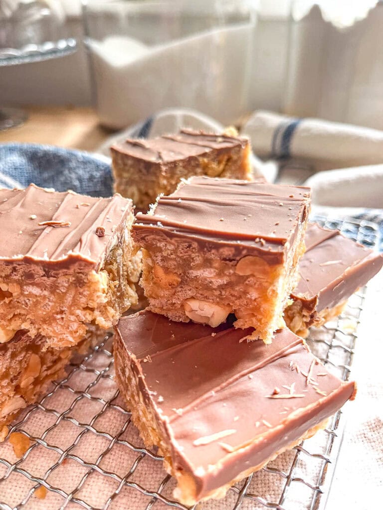 A stack of chew peanut butter Rice Krispie squares topped with chocolate on a small cooling wrap on top of a tea towel with a blue stripe.