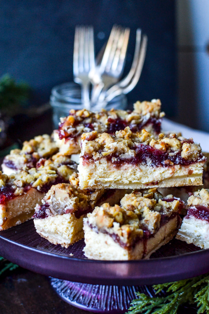 A plate of cranberry cheesecake bars with a jar of forks behind it
