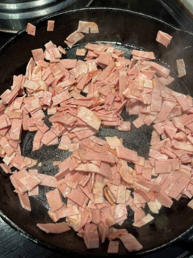 Chopped up turkey bacon frying in a cast iron frying pan.