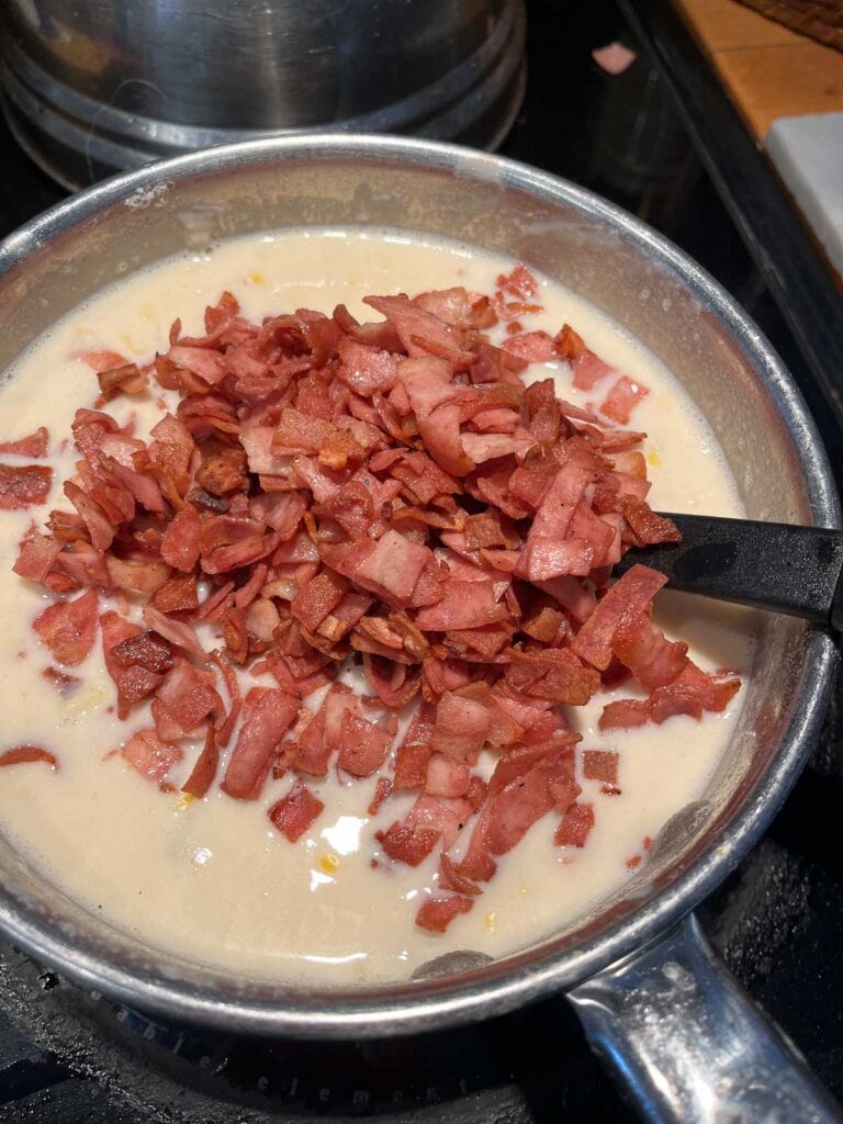 Crispy chopped bacon added to a pot of potato bacon soup with creamed corn.