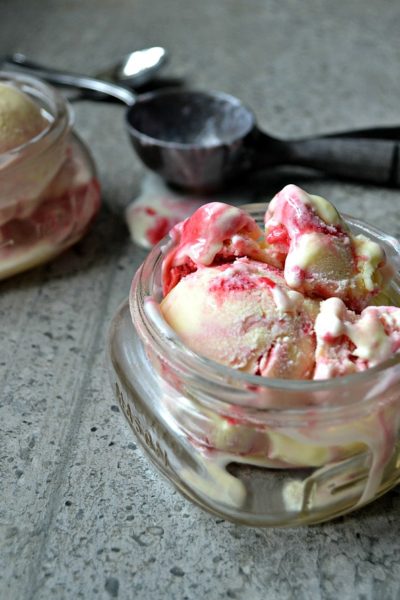 A small canning jar filled with raspberry swirl ice cream with an ice cream scoop on the side.