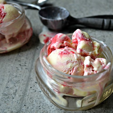 A small canning jar filled with raspberry swirl ice cream with an ice cream scoop on the side.