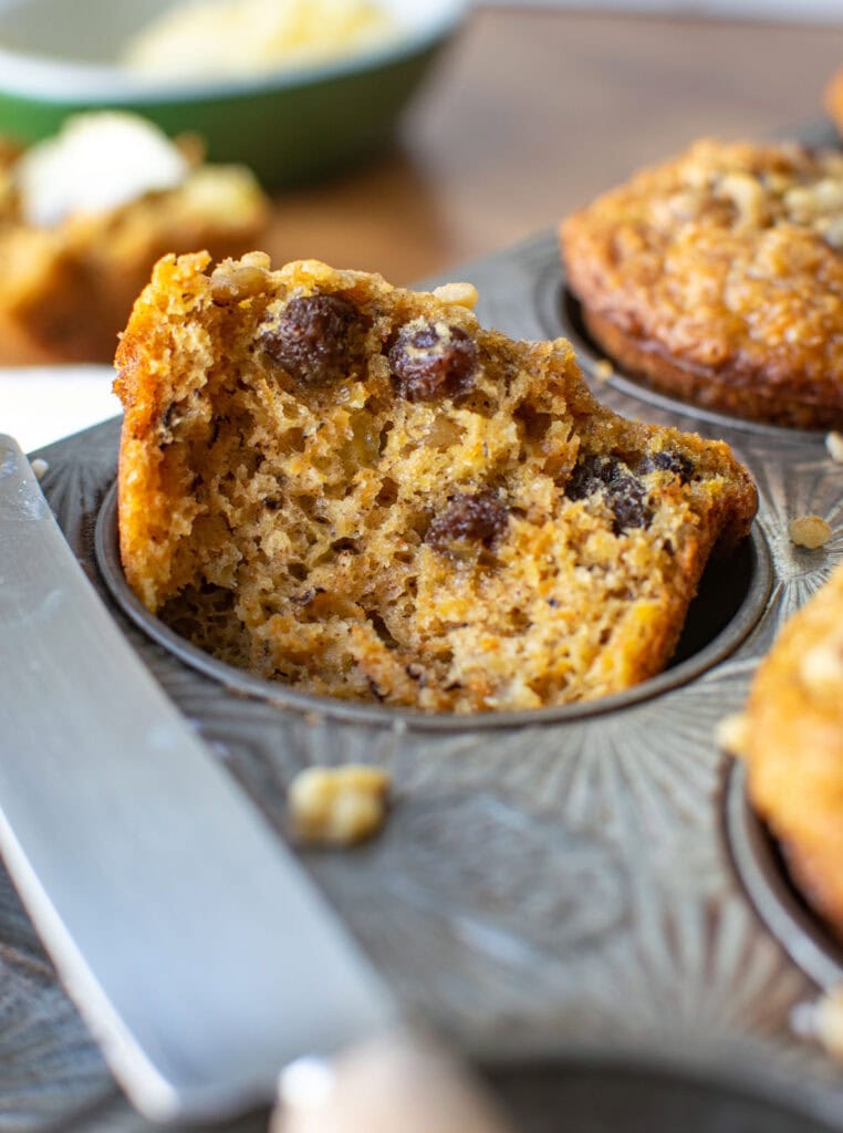 This image shows a close up of a morning glory muffin torn in half to show the inside, and resting in a muffin tin. 