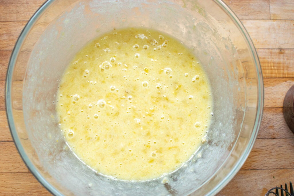 Sugar, eggs and vegetable oil added to mashed bananas in a large glass mixing bowl.