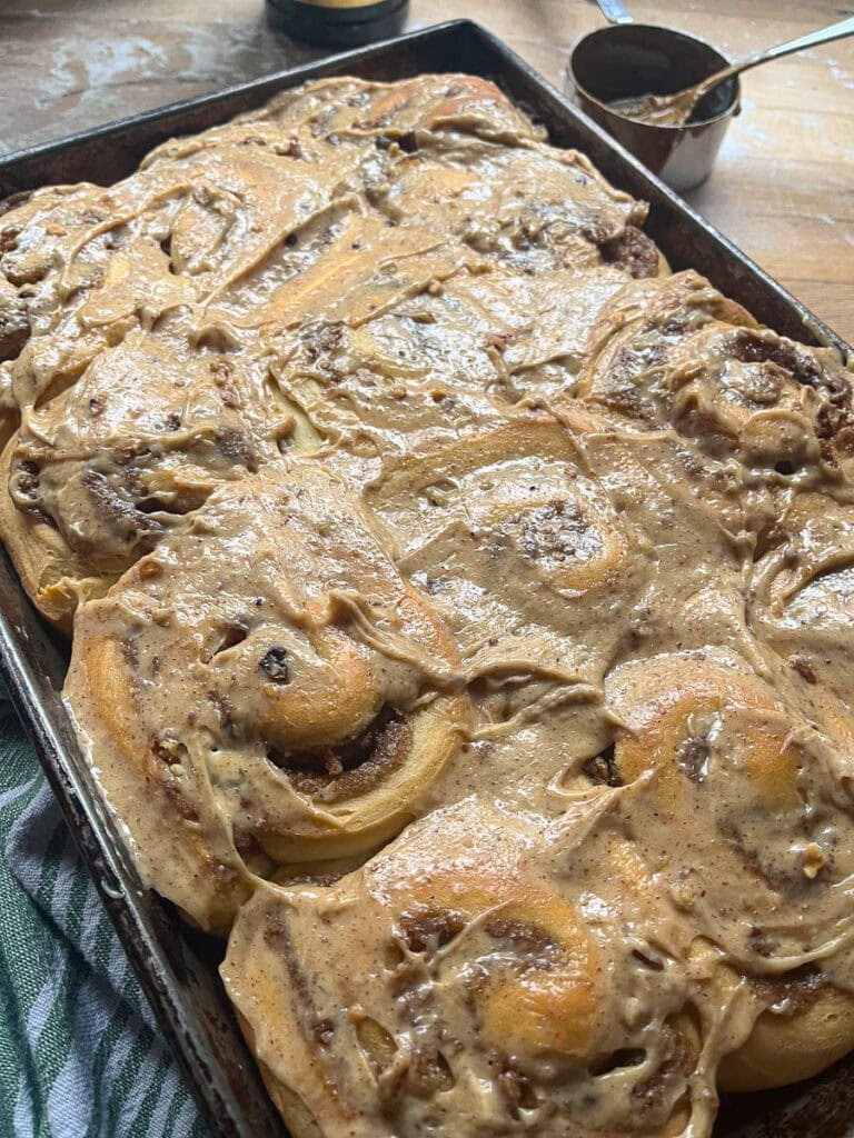 Freshly baked cinnamon rolls frosted with pecan cream cheese frosting while still warm in the pan.