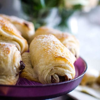 Freshly baked chocolate croissants on a purple cake plate.