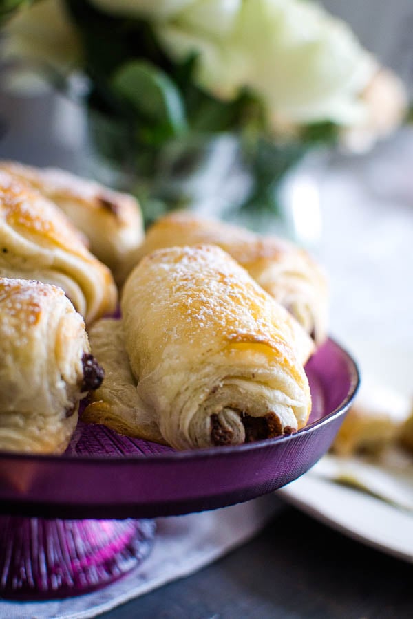 Freshly baked chocolate croissants on a purple cake plate.