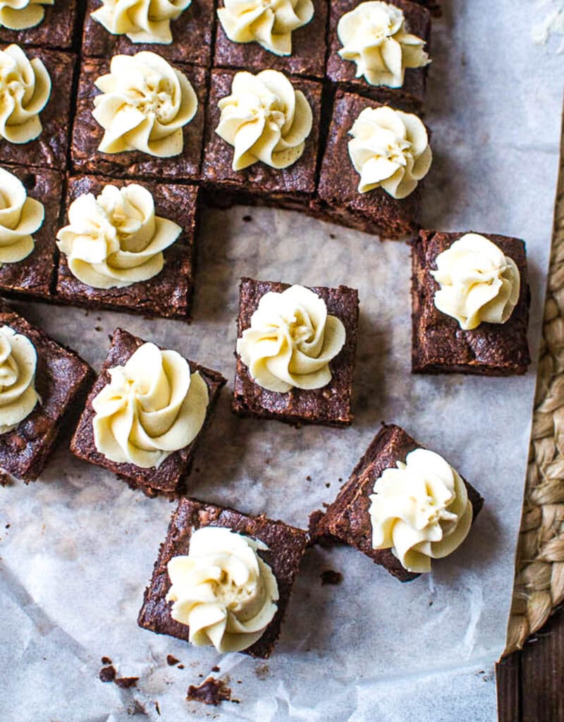 An overhead view of a parchment lined pan of mocha brownies with a frosted swirl on top of each square.