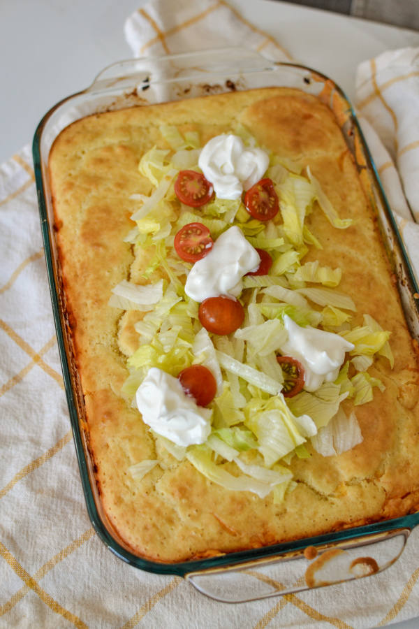 Taco casserole topped with chopped lettuce, sour cream and tomatoes
