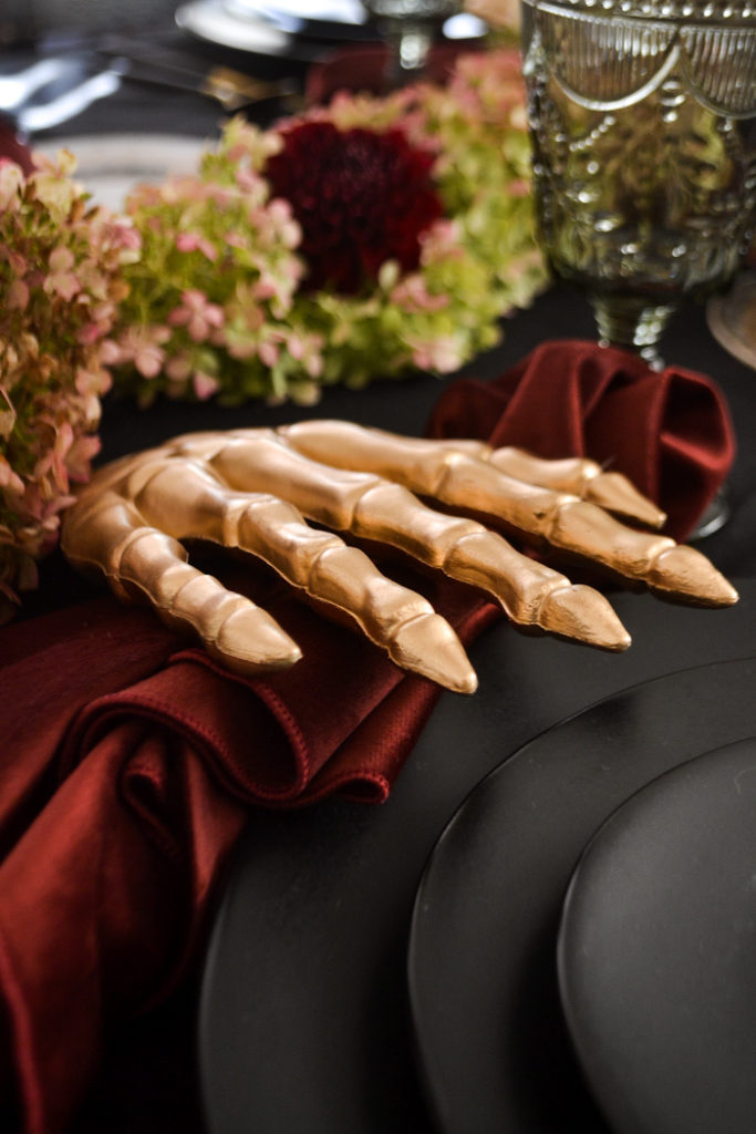 Gold painted skeleton hand holds a Merlot coloured velvet napkin