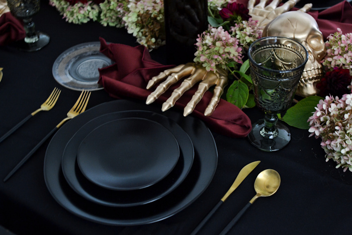 Black dinner plates, burgundy velvet napkin and gold skeleton hand