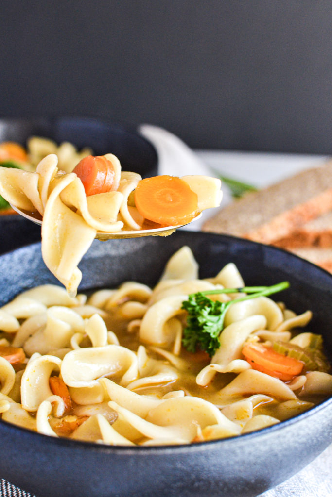 A spoon full of noodle soup with broth dripping into the bowl