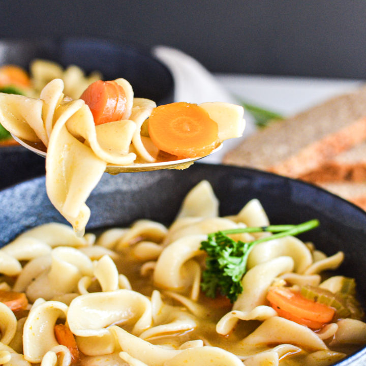 A fork full of noodle soup with broth dripping into the bowl