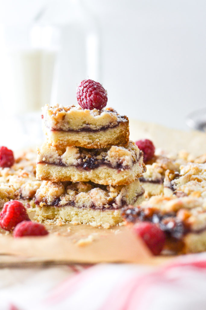 A stack of three raspberry squares, topped with a fresh raspberry and sprinkled with powdered sugar