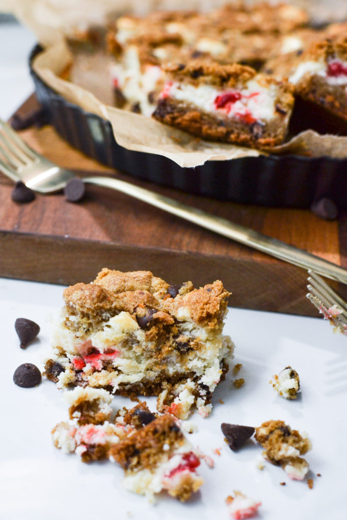 A half eaten chocolate chip cheesecake bar is pictured in front of several uneaten bars