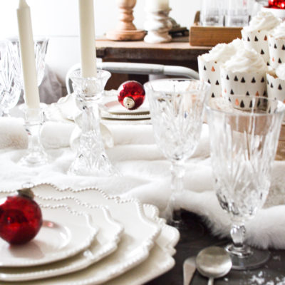 Two place settings of white plates on a table decorated all in white for Christmas