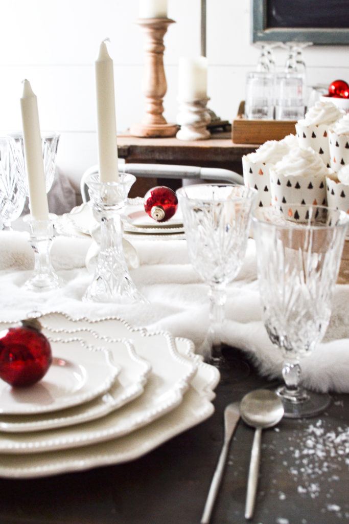 Two place settings of white plates on a table decorated all in white for Christmas