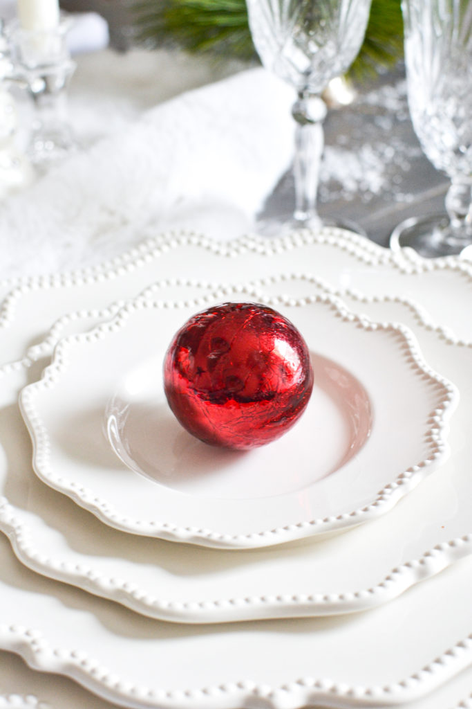 White Christmas tablescape with a stack of white plates and a red ornament on top