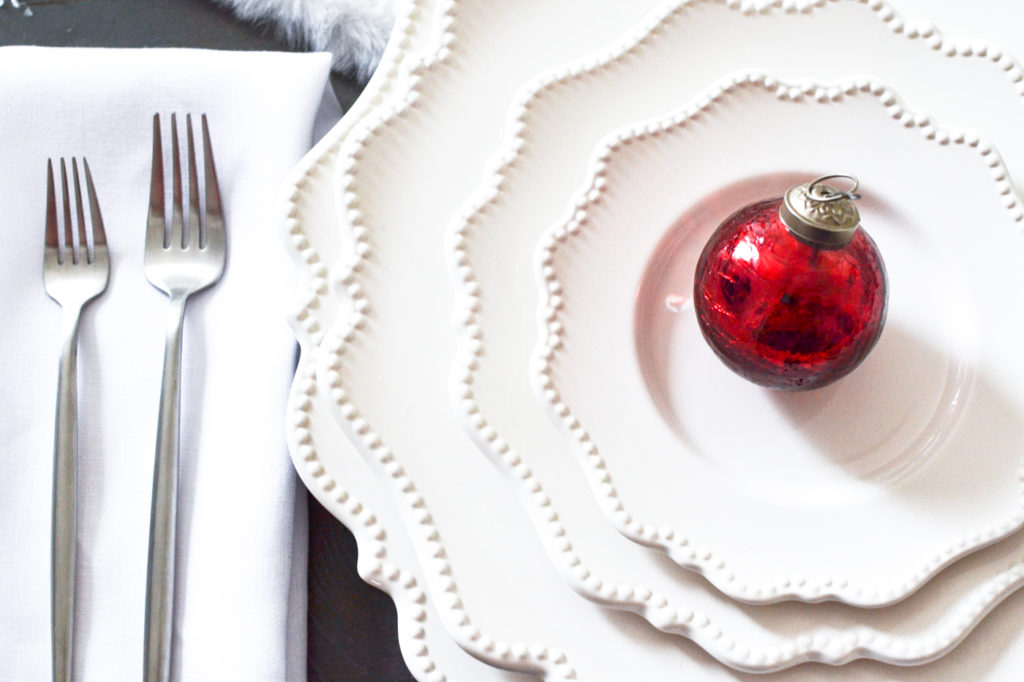 A stack of white plates with a red Christmas ornament