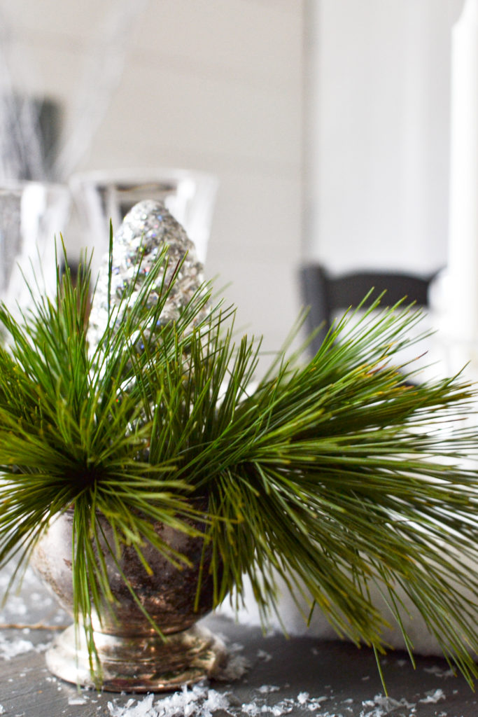 Small pieces of pine needles in a silver bowl with a silver pinecone ornament