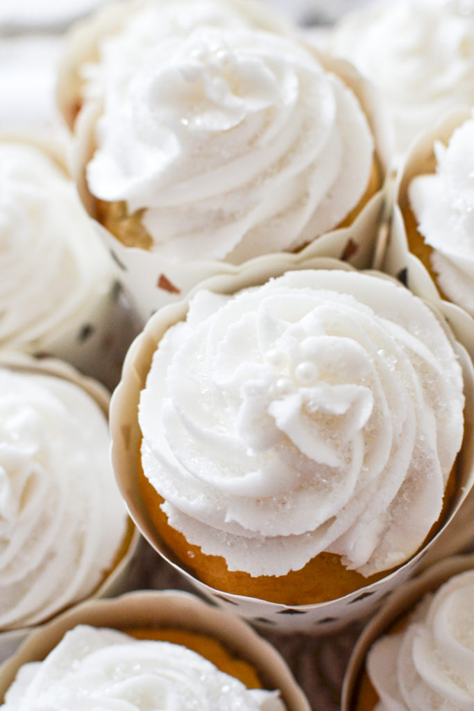 An overhead photo of white frosted cupcakes with tiny white edible beads