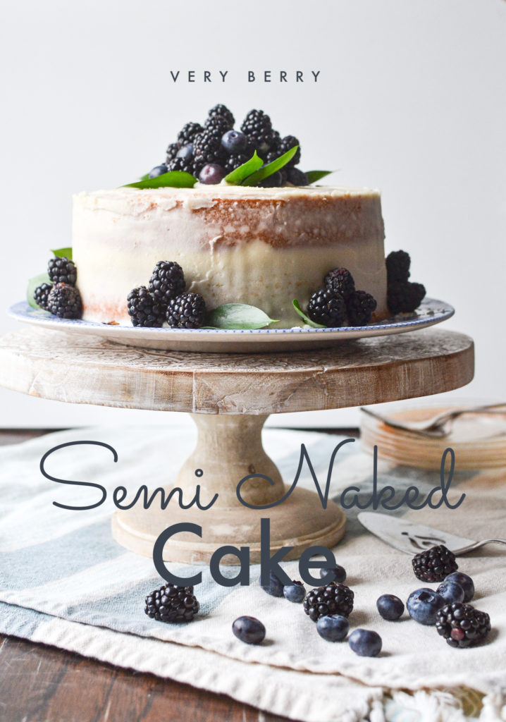 Semi naked cake decorated with berries on top of a wooden cake stand