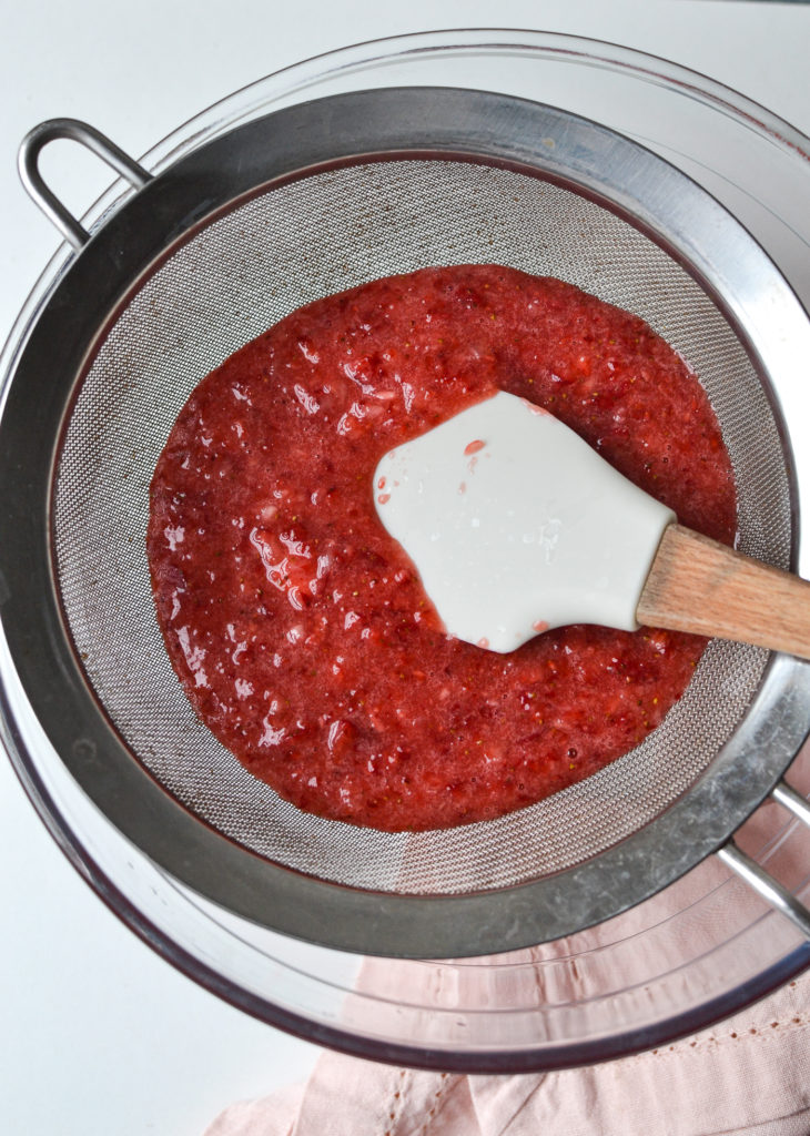 pureed strawberries being strained through a fine sieve