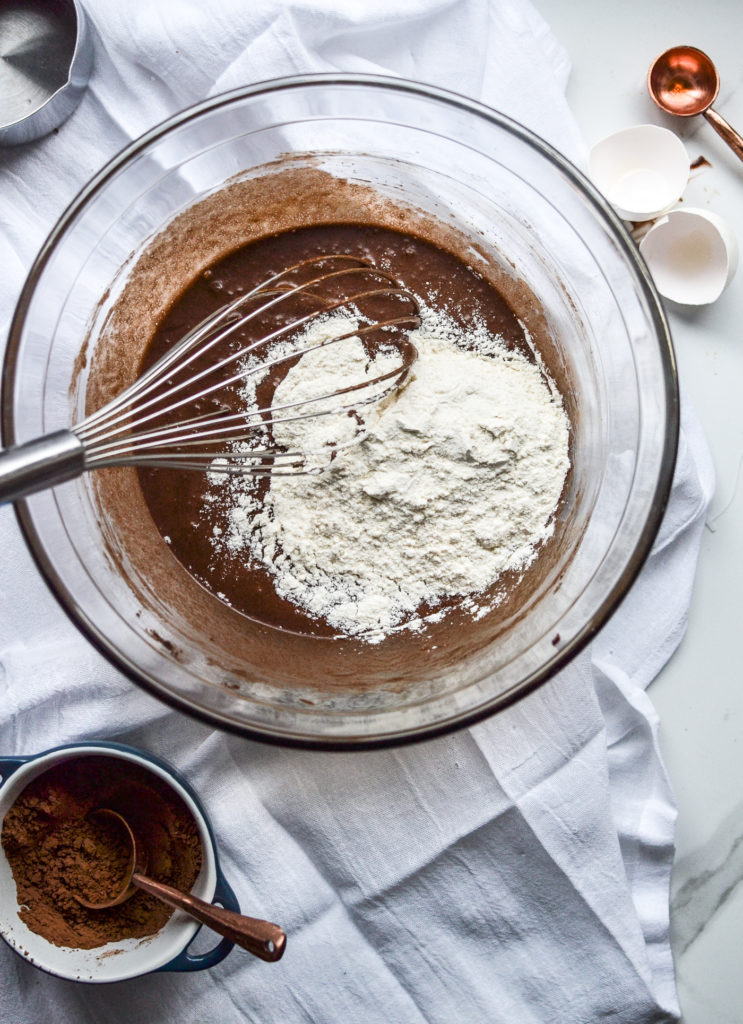 flour and baking powder being whisked into cocoa mixture for brownies