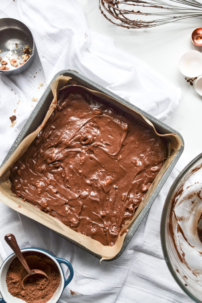 brownie batter in a parchment lined square baking pan as the base for marshmallow brownies