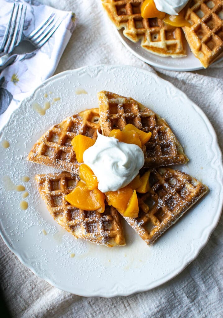 Waffles topped with peach sauce and a dollop of whipped cream on a white plate.