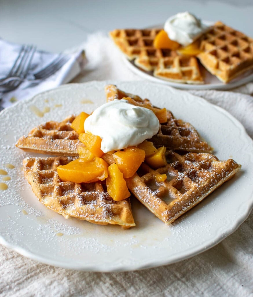 A peach waffle topped with peach sauce and fresh whipped cream.