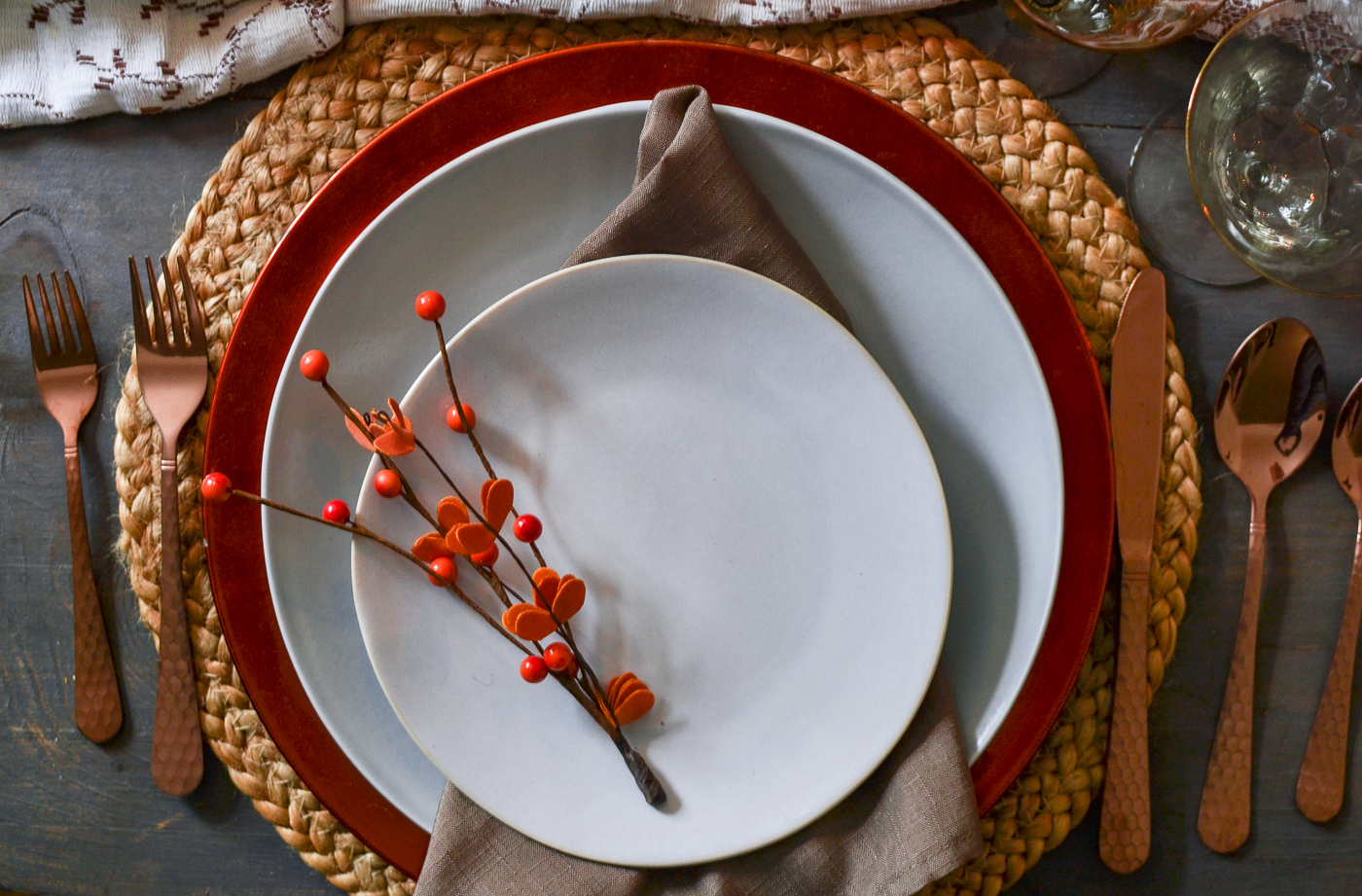 Autumn dinner table with soft blue and grey plates on top of an orange charger and rattan placemat.