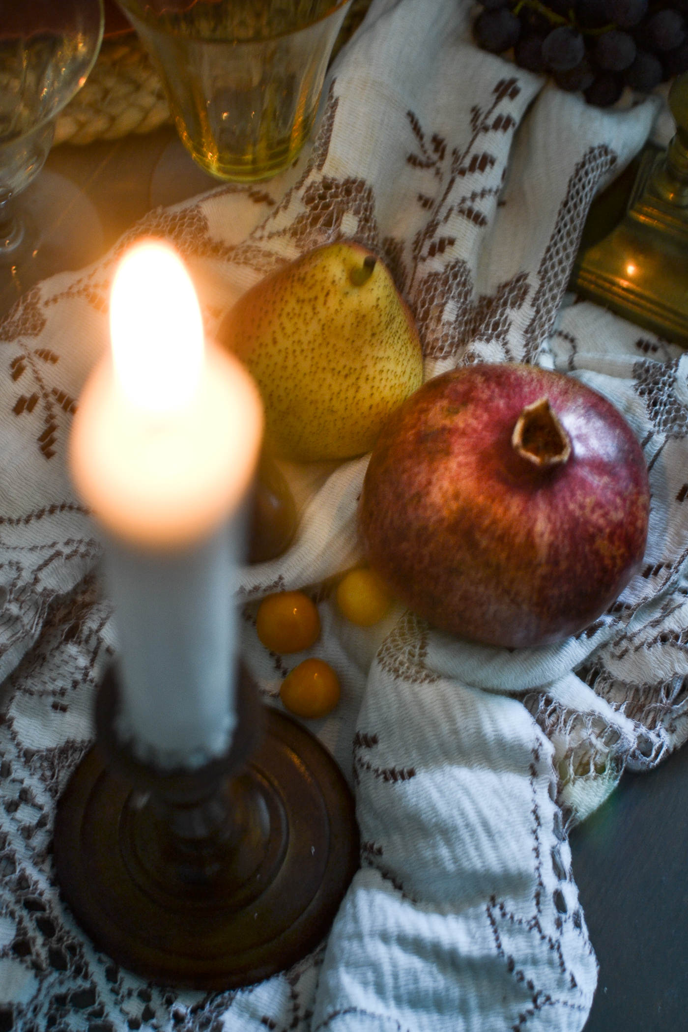 pomegranate and pear beside a burning candle on a dinner table set for autumn.