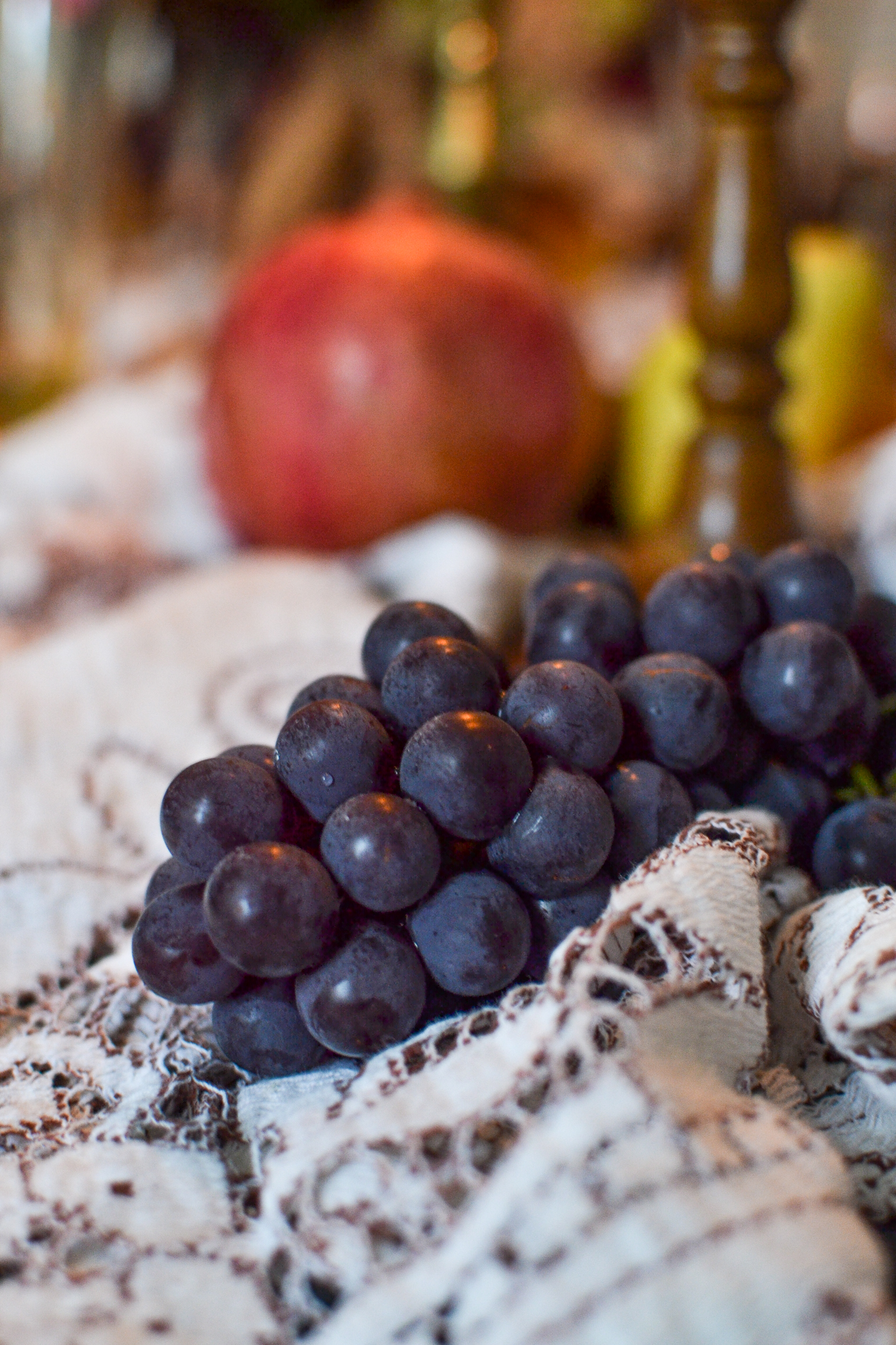 Fresh grapes and pomegranates on a lace table runner decorate a fall dinner table