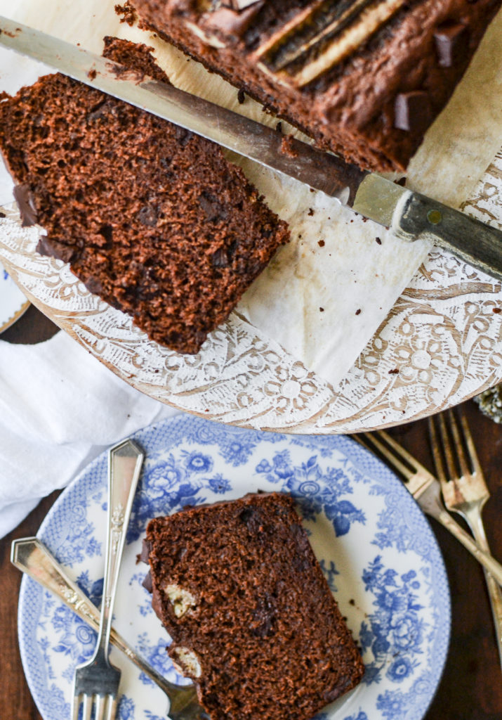 A loaf of chocolate banana bread with a freshly cut slice, and one slice on a blue and white plate.