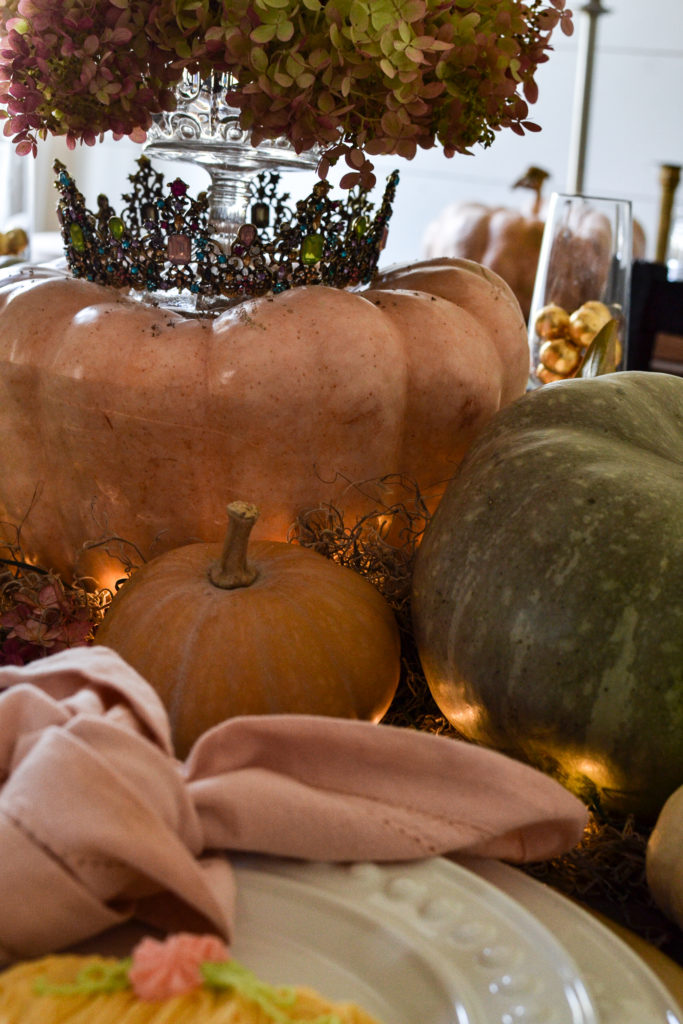 Pumpkins gather in the centre of a Halloween table. One is topped with a crown.