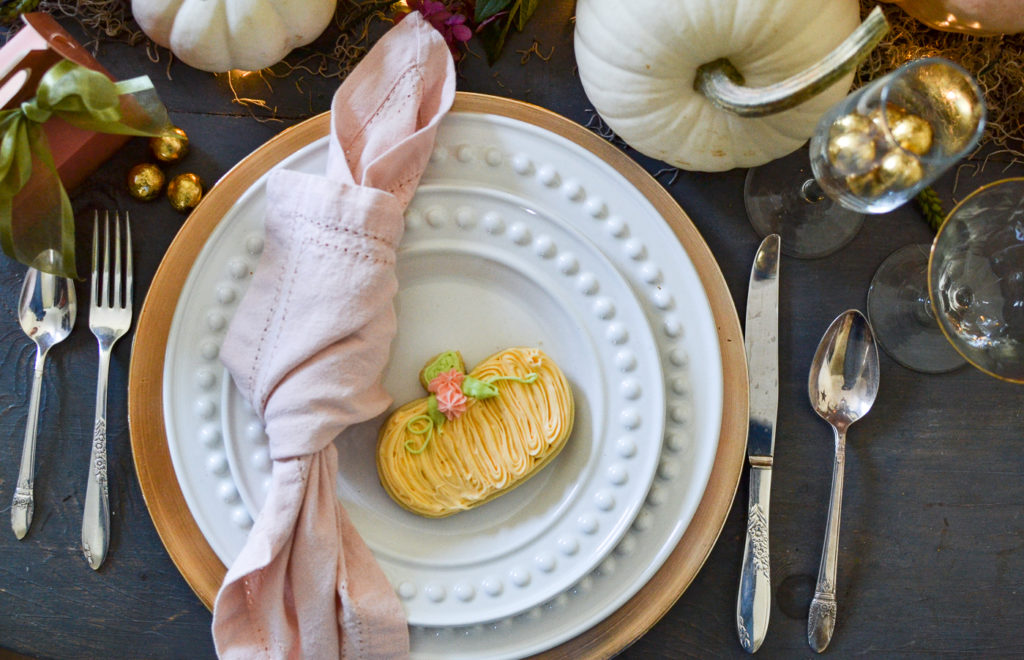 White plates on a gold charger with a pink napkin and pumpkin sugar cookie on top