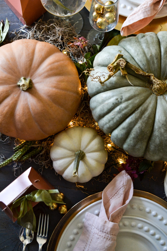 Overhead view of orange, white and blue/green pumpkins with twinkle lights tucked in between