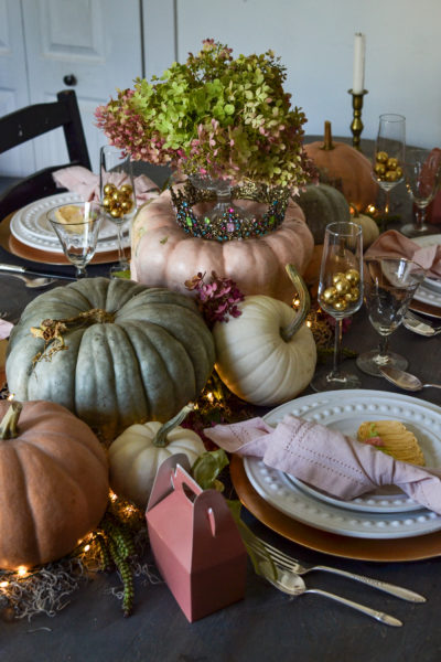 Real pumpkins in shades of pink, green, blue and white make a table runner down a dinner table styled for Halloween