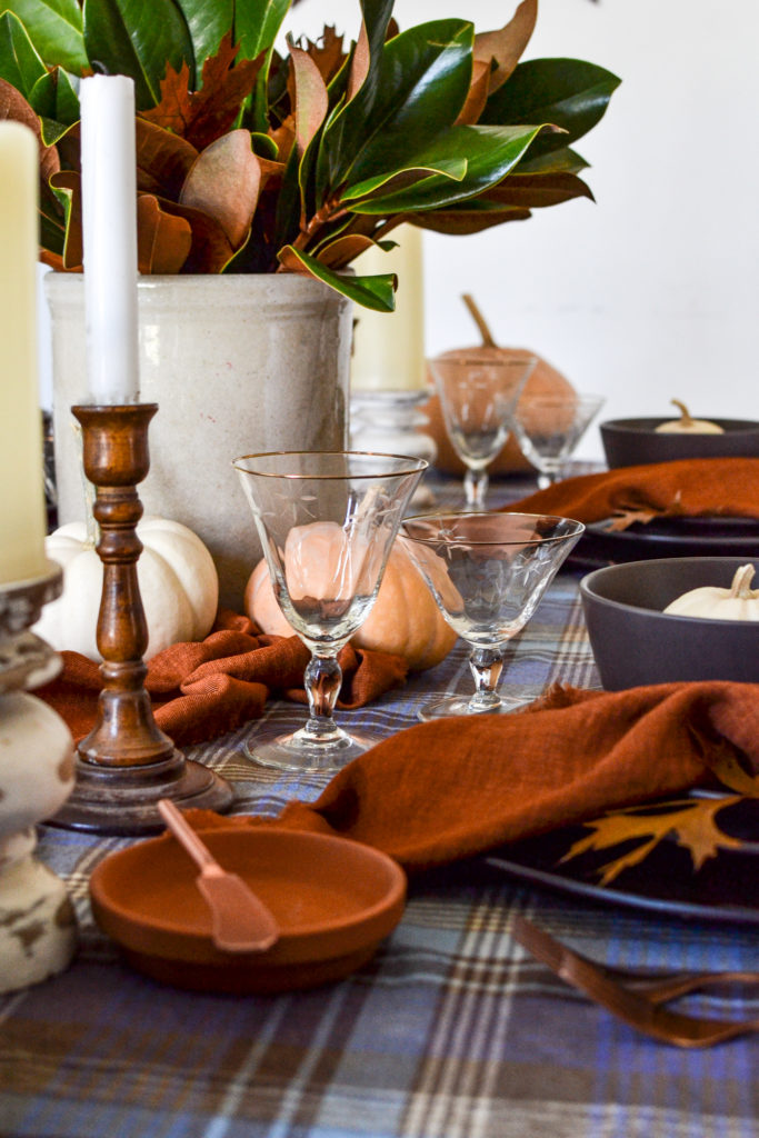 Wood candlestick beside a gold rimmed wine glass on a table set for the autumn season