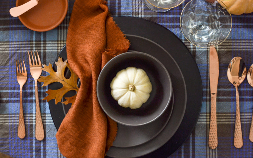 an overhead view of a plate setting on a cozy Thanksgiving table, with brown plates and a bowl with a tiny white pumpkin inside.