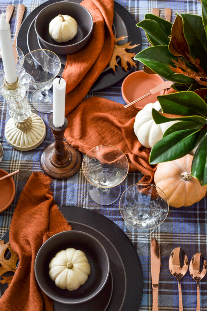 Overhead view of candles in wood and glass candlesticks and gold rimmed wine glasses, with terracotta colored napkins.