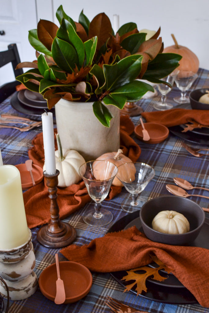 Simple Thanksgiving table decor in shades of blue, terracotta and brown including pumpkins, leaves and magnolia branches.