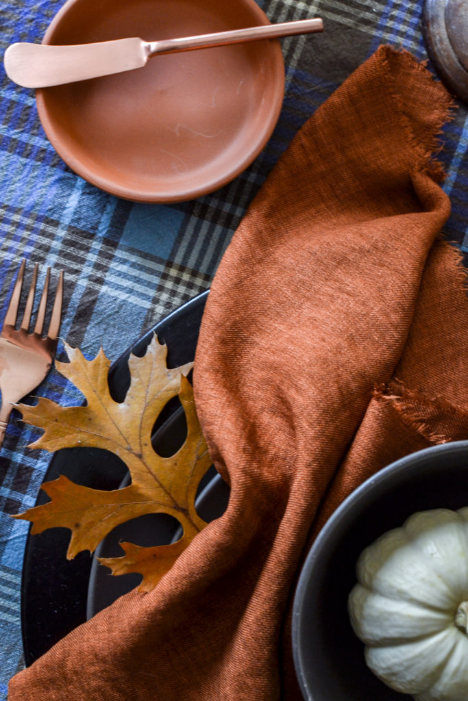 An oak leave tucked under an orange napkin on a fall tablescape.