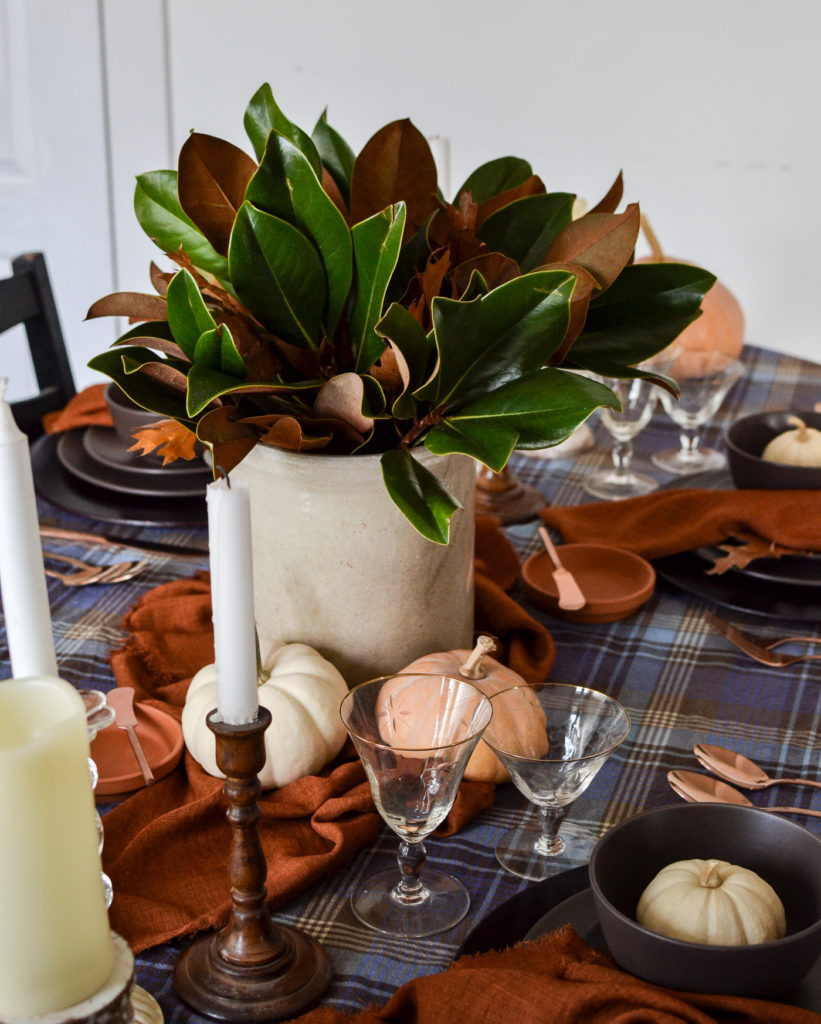 A crock filled with magnolia leaf branches as a centerpiece on a cozy Thanksgiving tablescape