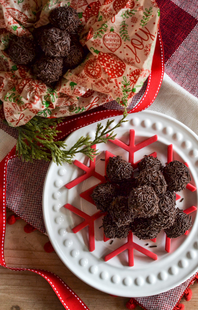 An overhead view of a plate of rum balls, and a few extras piled in a festive tissue lined box.